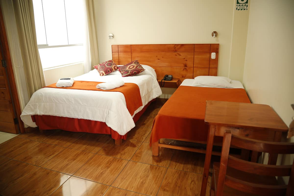 Habitación de hotel con dos camas, un cabecero de madera, una mesita y una silla.