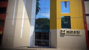 A modern building with a yellow and white facade, a glass entrance, and a sign reading "MUNAYKI". - Munayki Hotel (Tacna)