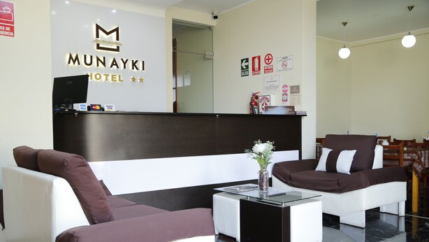 A reception area with a reception desk, two sofas, a coffee table, and a vase with flowers. - Munayki Hotel (Tacna)
