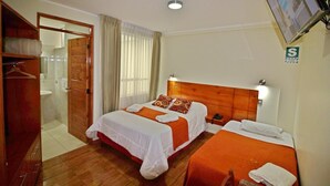 A hotel room with two beds, a wooden wardrobe, a shower area, and a television mounted on the wall. - Munayki Hotel (Tacna)