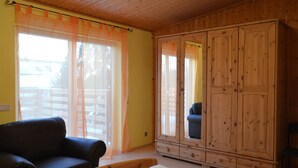 A bedroom with a bed, a wooden wardrobe, a sofa, and a window with curtains. - Wunderschone Ferienwohnung im Burgenland (Manderscheid)