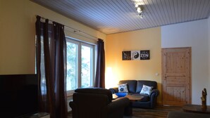 A living room with a TV, sofa, and a wooden floor. - Wunderschone Ferienwohnung im Burgenland (Manderscheid)