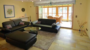 A living room with a black sofa, a glass coffee table, and a beige rug. There is a dining area with wicker chairs and a table. - Apartment With Private Terrace in Prunn (Riedenburg)