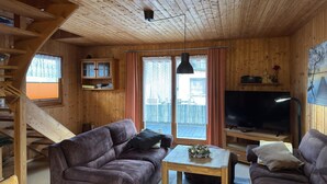 L’intérieur d’un chalet en bois, avec un canapé, une petite table, un téléviseur, un escalier et une fenêtre avec des rideaux.