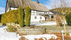 A traditional house with a steep roof, stone wall, and a well-maintained garden with evergreen shrubs. - Flat Near the ski Area in Medebach (Medebach)