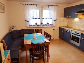 A compact kitchen with a dining area, featuring a wooden table, chairs, a built-in oven, and a window with curtains. - Flat Near the ski Area in Medebach (Medebach)