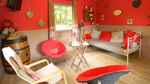 A room with a red wall, a bed with red and white bedding, a wooden barrel, a red chair, a small table, and a window with curtains. - Chalet in a Green and Peaceful Environment (Houffalize)