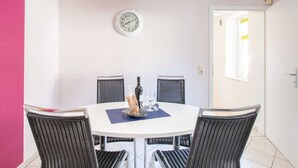 A dining area with a round table, four wicker chairs, a clock on the wall, and a window with a view. - Wohnung in der Nahe des Skigebietes Battenberg (Battenberg)
