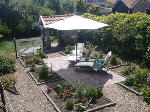 Pátio com mesa e cadeiras, cercado por plantas e uma estrutura de tijolos.