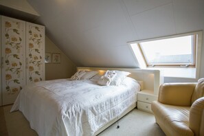 Um quarto com cama, mesa de cabeceira, cadeira, guarda-roupa e claraboia.