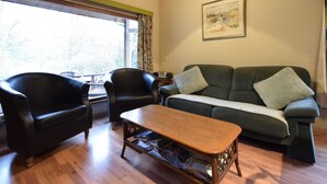 A living room with a wooden coffee table, two black leather chairs, a green sofa, and a large window with curtains. - Forest Cottage With Ponds (Bouillon)