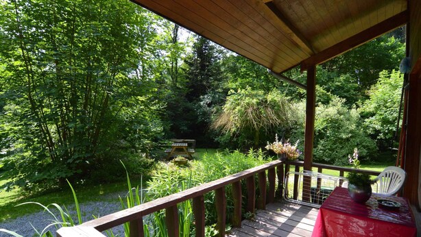 A wooden deck with a table and chairs, surrounded by lush greenery and trees. - Forest Cottage With Ponds (Bouillon)