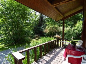 A wooden deck with a table and chairs, surrounded by lush greenery and trees. - Forest Cottage With Ponds (Bouillon)
