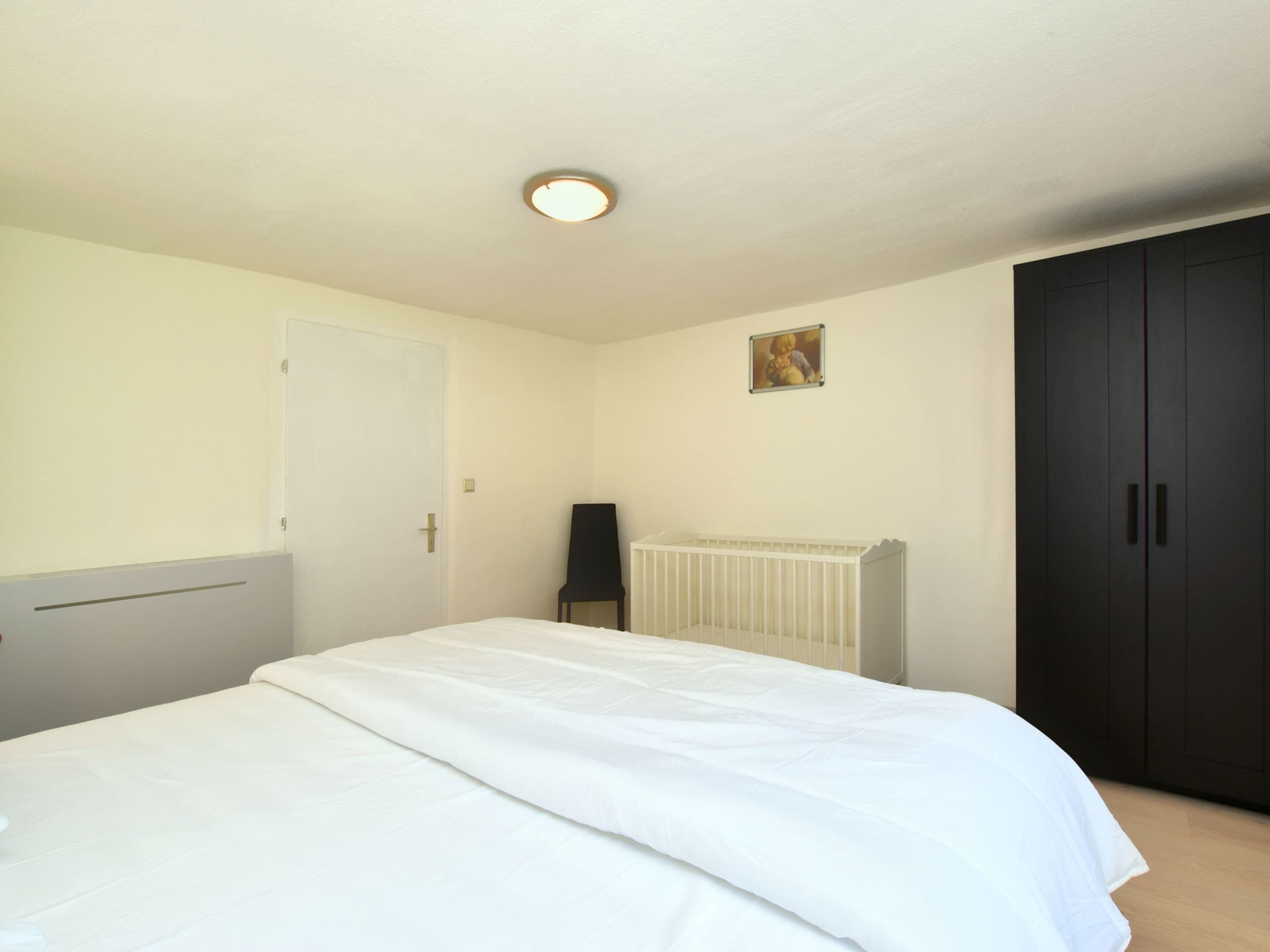 A bedroom with a bed, a radiator, a door, and a dark wardrobe.