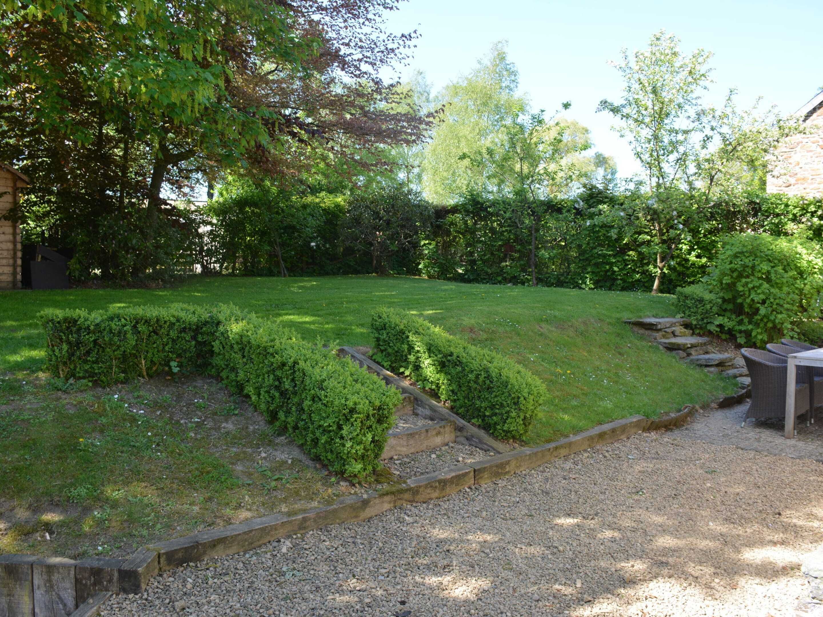 Ein gepflegter Garten mit Kiesweg, ordentlich geschnittenen Hecken und einer Sitzgelegenheit mit Holzbank.