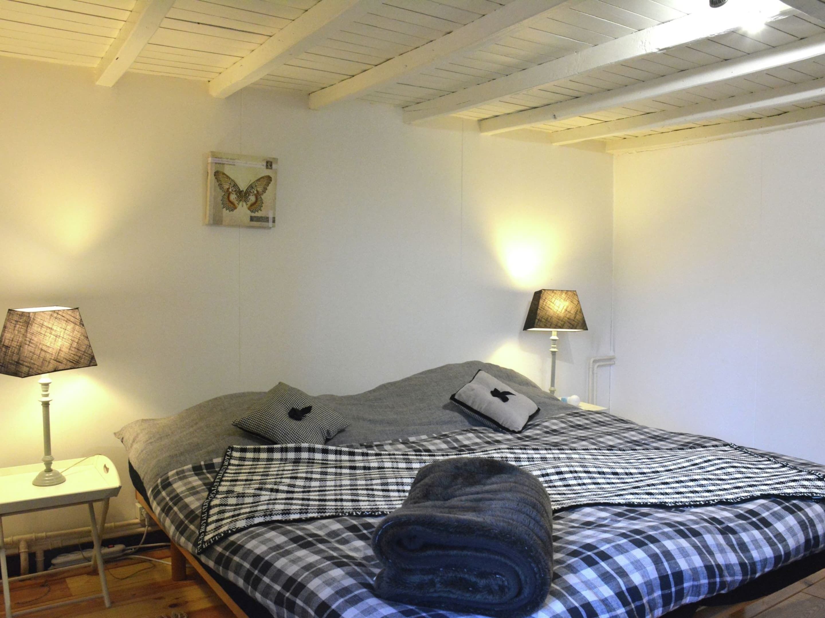 A bedroom with a bed, two bedside lamps, a wall-mounted picture, and a small table with a lamp.