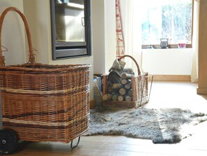 Une pièce comprenant un grand panier en osier, un panier en osier plus petit rempli de bûches, un tapis en fourrure et une fenêtre avec des rideaux.