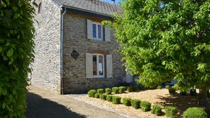A stone building with a gravel driveway, a small garden with trimmed bushes, and a tree to the right.