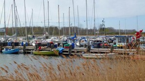 Een jachthaven met verschillende boten die aanmeren, omringd door hoog gras en een heldere lucht.