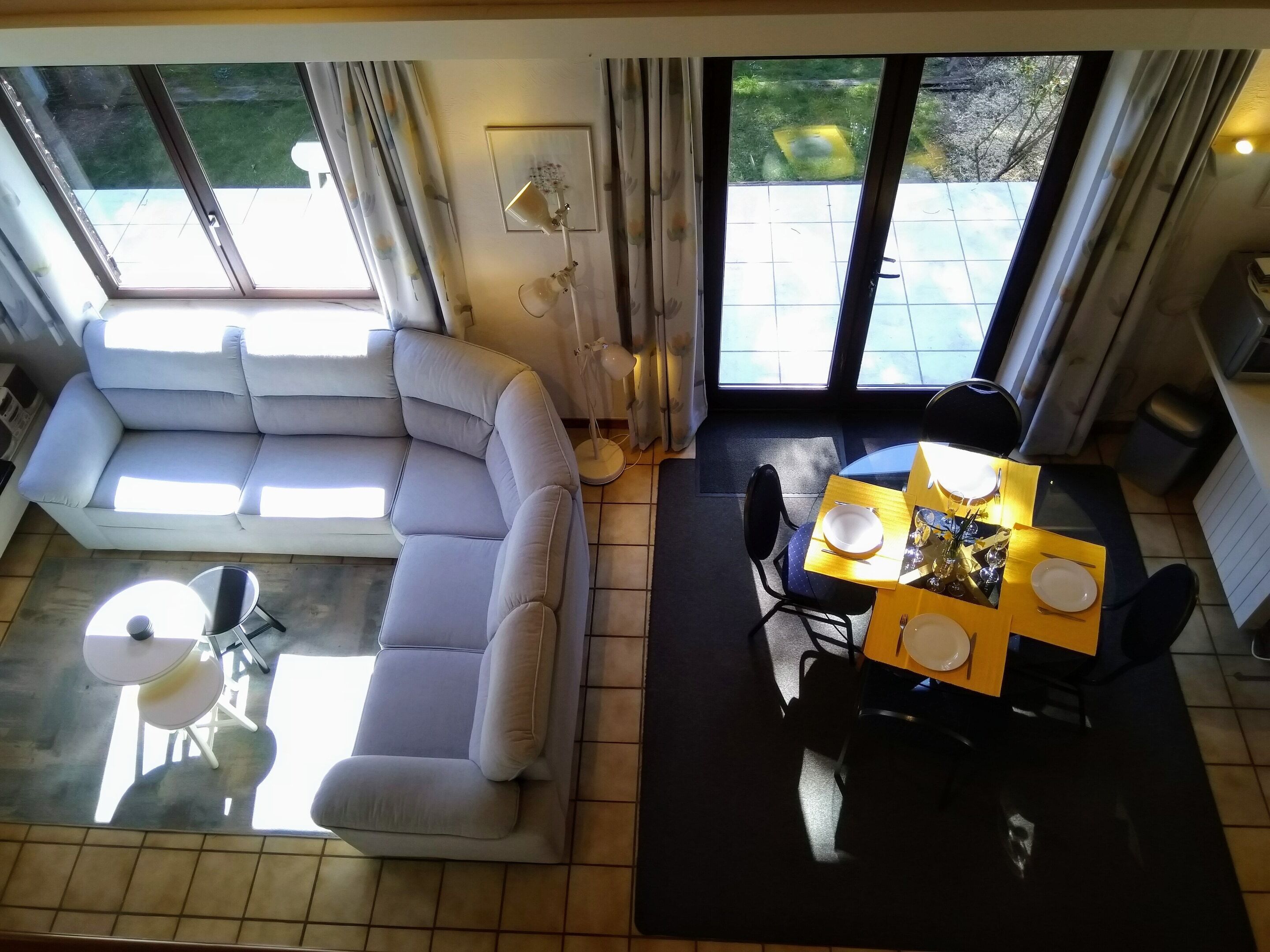 A living room with a sofa, a dining table with chairs, a small round table, and a ceiling fan.