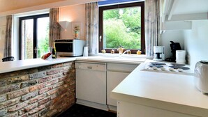 Een keuken met een bakstenen muur, een vaatwasser, een magnetron, een koffiezetapparaat en een raam met gordijnen.