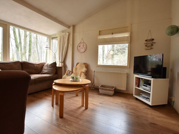 A cozy living room with a brown leather sofa, a wooden coffee table, a television on a white stand, and a window with curtains.