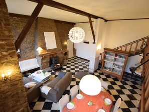 A cozy room with a checkered floor, a fireplace, a dining table set for four, and a staircase with wooden railings. - Charming House, Perfect for Family Holidays (Erezee)