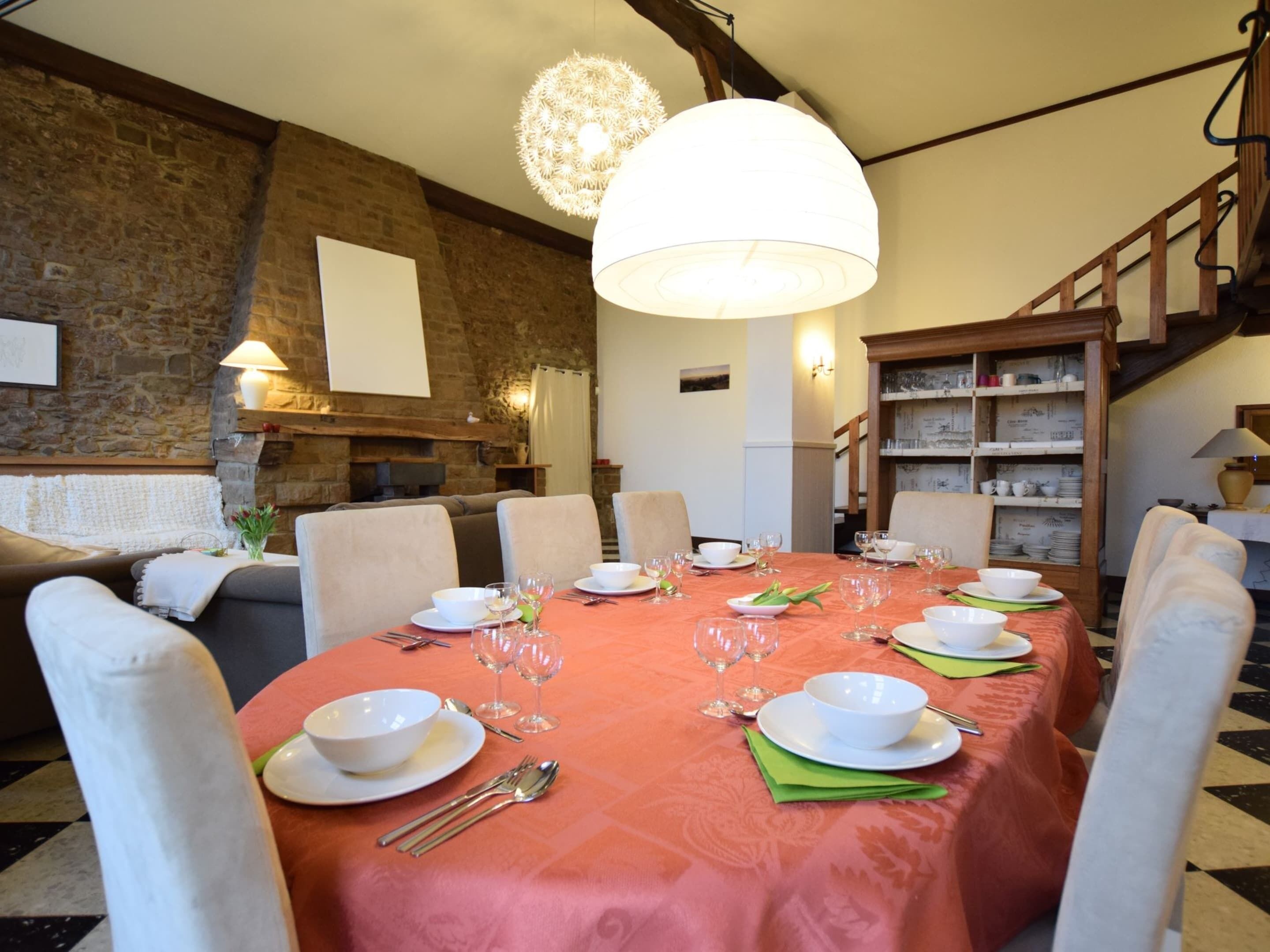 A dining area with a brick wall, a large chandelier, and a wooden staircase.