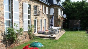 Une maison en pierre avec des volets blancs, une terrasse avec une table et des chaises, et un parasol vert.