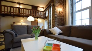 Un salon chaleureux avec une table basse blanche, deux canapés, un vase de fleurs et un mur en pierre.