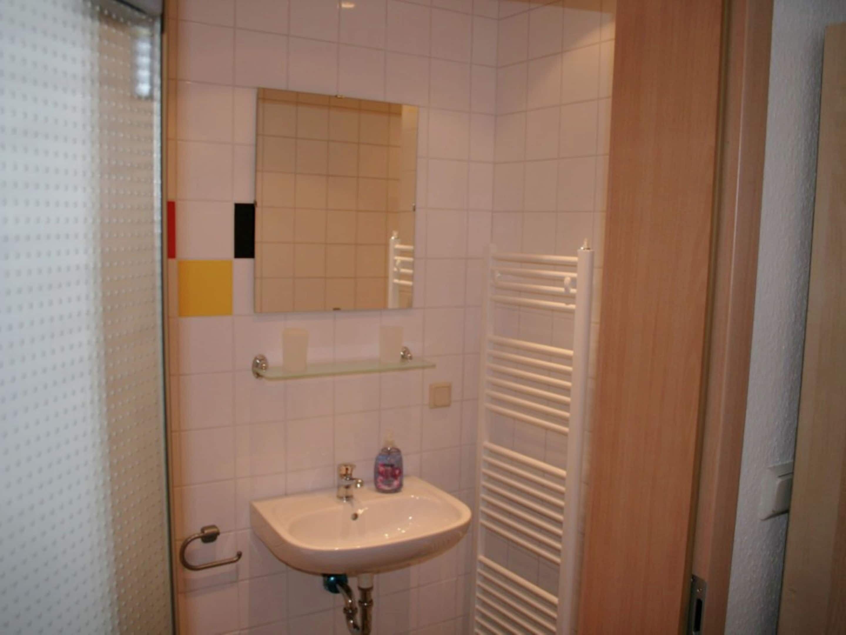 Un baño con lavamanos, espejo y toallero.