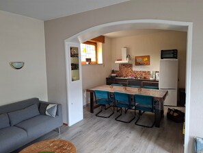 Um espaço de estar compacto com cozinha compacta, área de jantar com cadeiras azuis, sofá cinza e mesa redonda pequena.