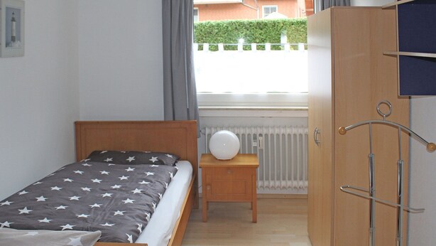 A bedroom with a bed, a nightstand, a wardrobe, and a window with curtains. - Apartment in Bodenwerder mit Balkon (Bodenwerder)