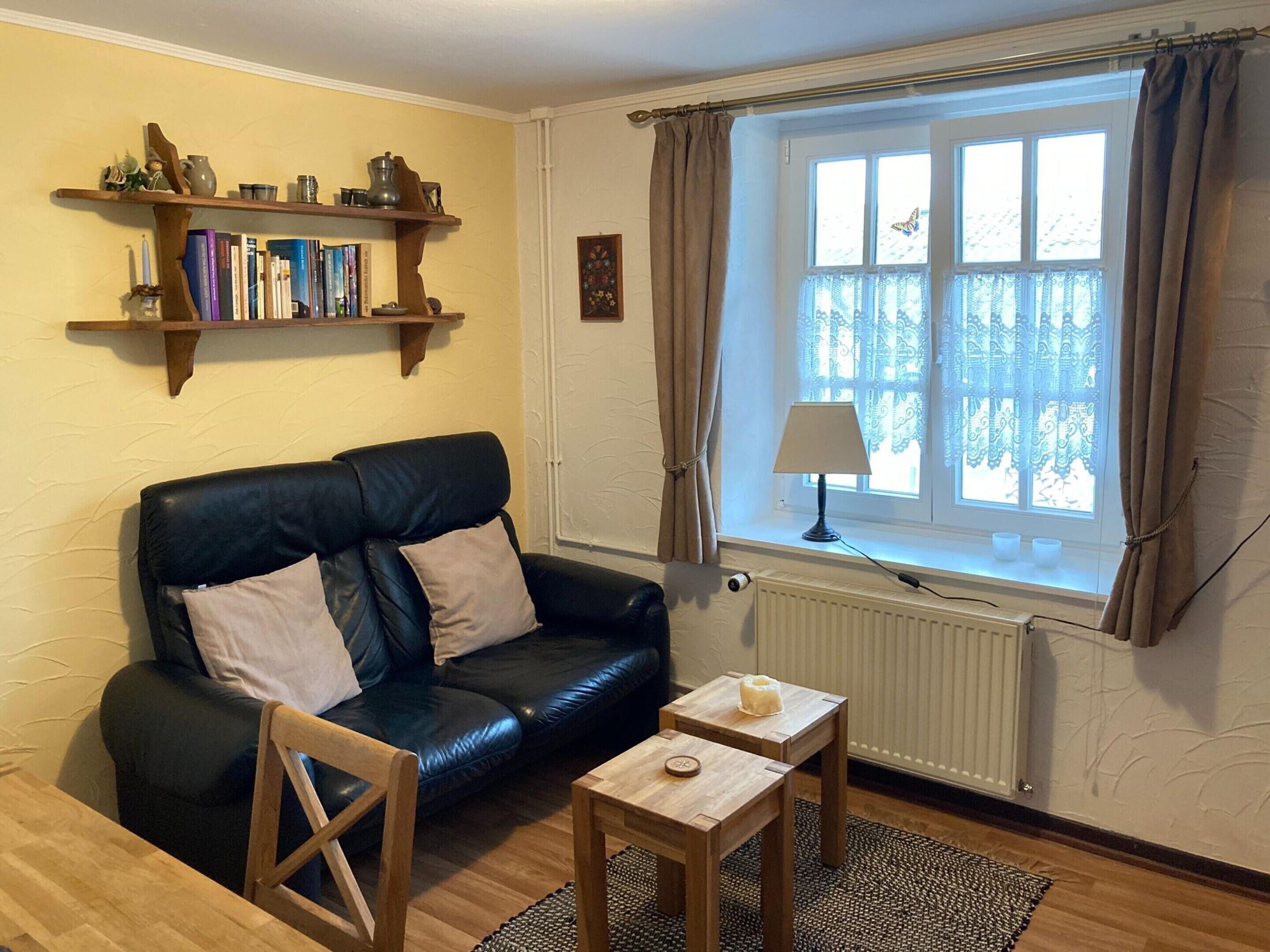 A cozy living room with a leather sofa, a wooden coffee table, a bookshelf, and a window with curtains.
