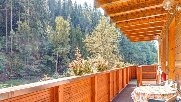 A wooden deck with a table and chairs, overlooking a forested area.