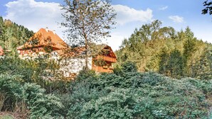 A rustic building with a sloped roof, surrounded by dense greenery and trees.