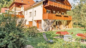 A two-story wooden house with a balcony, a covered porch, and a garden with outdoor furniture.