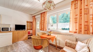 A cozy living room with a sofa, a dining table with chairs, a television, and a kitchen area with a microwave and a toaster.