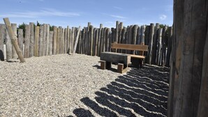 A wooden bench in a gravel area with a wooden fence in the background. - Apartment Near Groote Keeten Beach (Callantsoog)