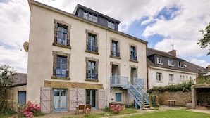 Ein mehrgeschossiges Gebäude mit Balkon, Treppe und einem kleinen Gartenbereich mit Blumen.