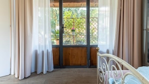 Una stanza con un letto, una finestra con tende, un soffitto in legno e vista sul verde.