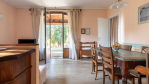 Un'accogliente stanza con un tavolo da pranzo in legno, sedie, una TV e vista su uno spazio esterno attraverso una porta vetrata.