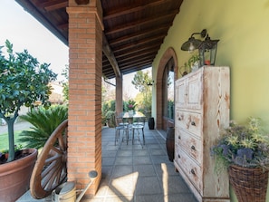 A covered patio area with a brick column, a wooden table with chairs, a vintage dresser, and potted plants.