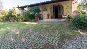 Una casa con tetto in tegole, ingresso in mattoni e vialetto lastricato che conduce a un portico con una sedia e un tavolo.