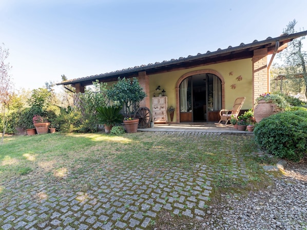 A house with a tiled roof, a brick entrance, and a paved driveway leading to a porch with a chair and a table.