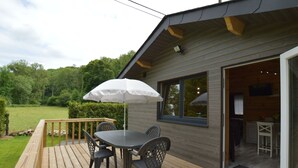 A wooden deck with a table and chairs, an umbrella, and a view of a green landscape. - Chalet Near Durbuy With Private Garden (Ferrieres)