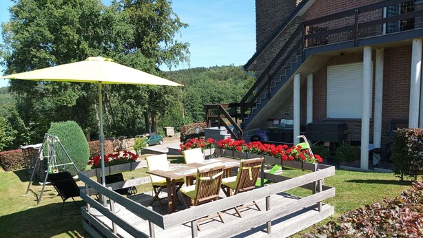 An outdoor patio area with a wooden table and chairs, a swing set, and a yellow umbrella. - Peaceful Escape, Malmedy (Malmedy)
