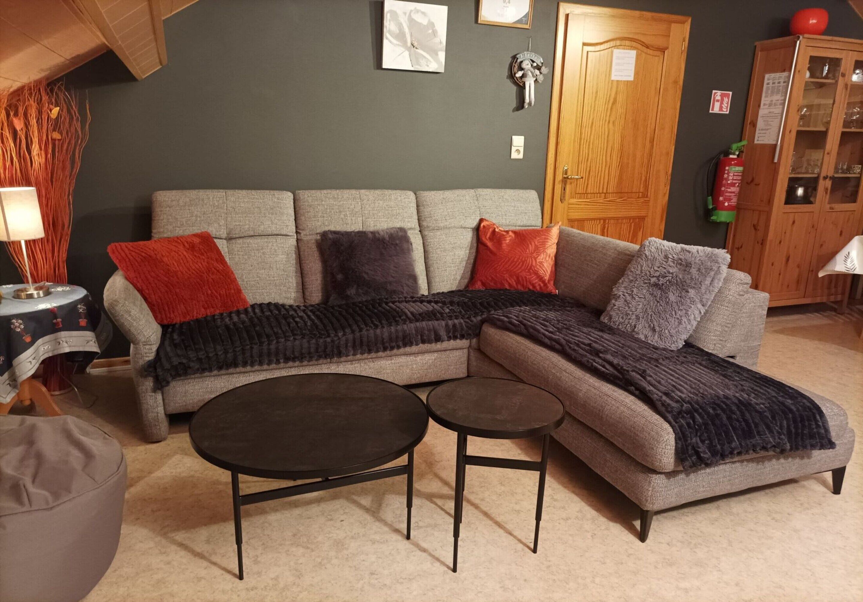 Ein Wohnzimmer mit Ecksofa, zwei Beistelltischen, einem runden Couchtisch und einer Vitrine.