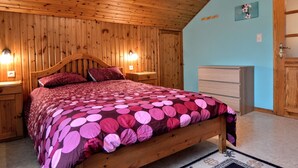 A bedroom with a wooden ceiling, a bed with a patterned bedspread, a nightstand, a dresser, and a door. - Peaceful Escape, Malmedy (Malmedy)