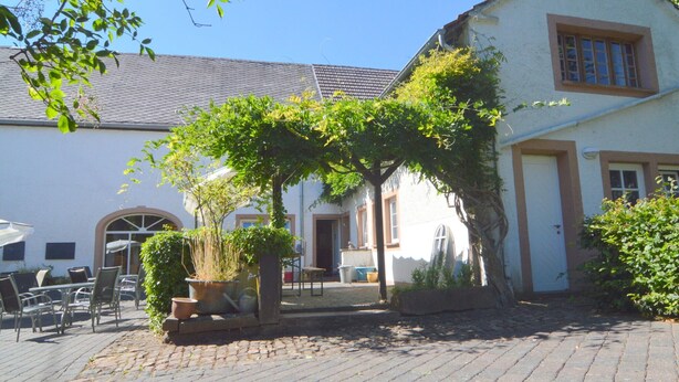 A courtyard with a building, outdoor seating, and potted plants. - Apartment Near the Forest in Meisburg (Meisburg)